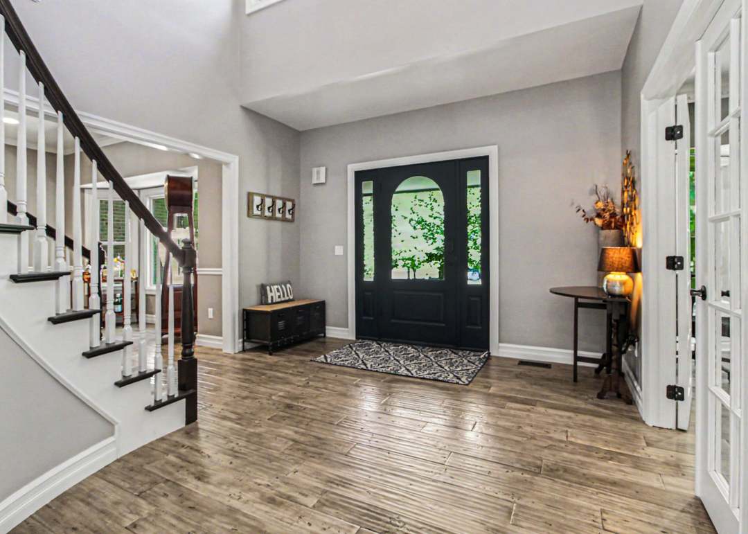 The two-story entry foyer with a curved staircase, dark front door with arched glass, and wide-plank wood-look floors.