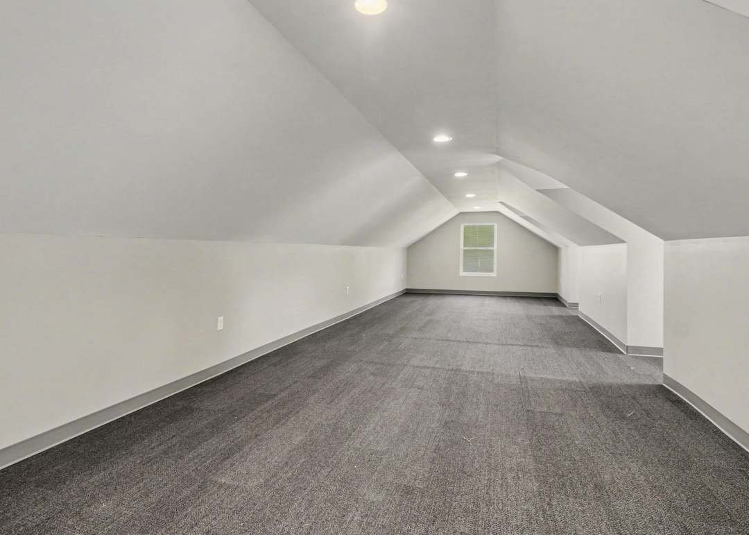 The finished flex room above the detached garage, a bright vaulted space with dormer windows and dark carpet.