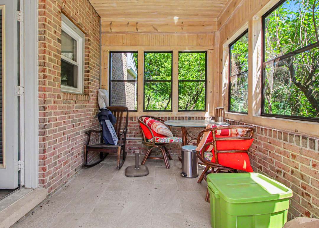 The three-season porch with brick walls, a wood-plank ceiling and screened windows looking out into green trees.