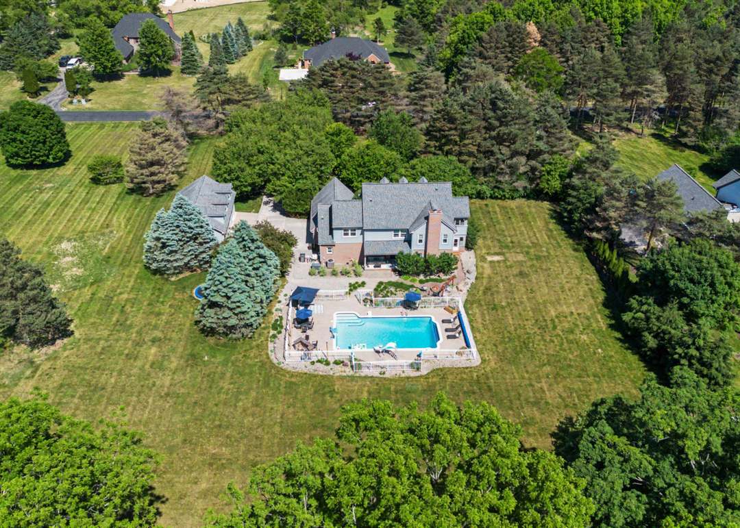 Aerial view of 5875 Pinecrest Estates Drive: the brick Colonial, its inground pool and paver patio, set on two private acres of lawn ringed by mature trees.